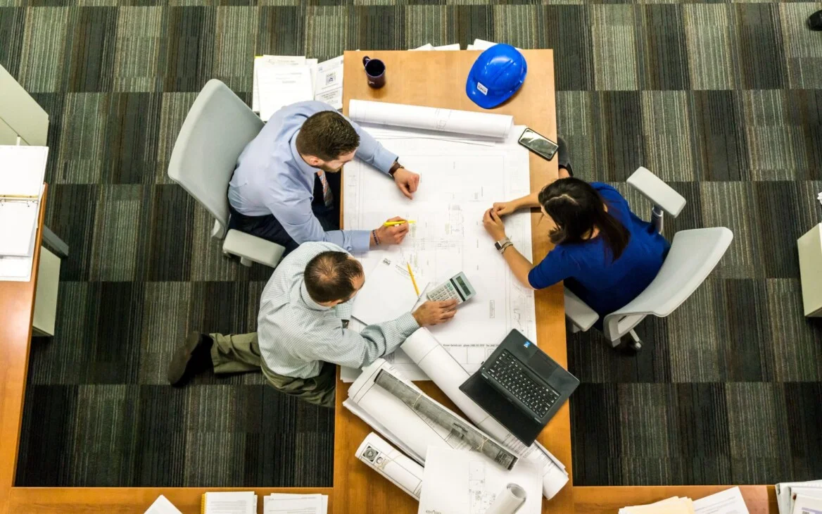 Photo prise au-dessus d'une table avec deux hommes qui font face à une femme au-dessus d'un plan d'architecte.