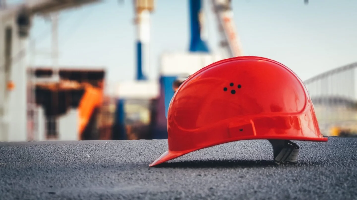 Photo d'un casque rouge au premier plan avec un chantier dans en arrière plan.